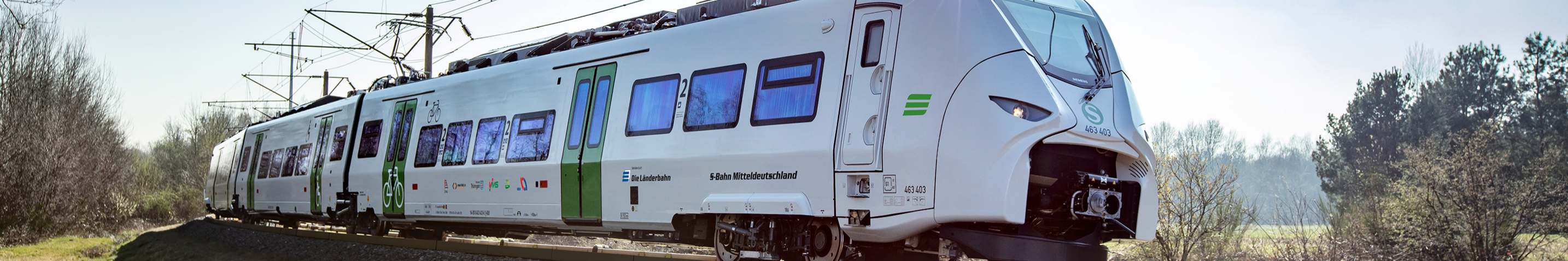 Auf dem Bild ist der Siemens Mireo von der Seite zu sehen. Er fährt durch eine karge Landschaft. Er ist mit dem Logo der Länderbahn sowie dem Schriftzug S-Bahn Mitteldeutschland beklebt.