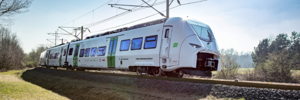 Auf dem Bild ist der Siemens Mireo von der Seite zu sehen. Er fährt durch eine karge Landschaft. Er ist mit dem Logo der Länderbahn sowie dem Schriftzug S-Bahn Mitteldeutschland beklebt.