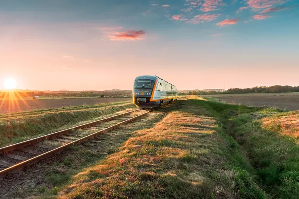 Der trilex fährt durch eine grüne Landschaft und links geht die Sonne auf.