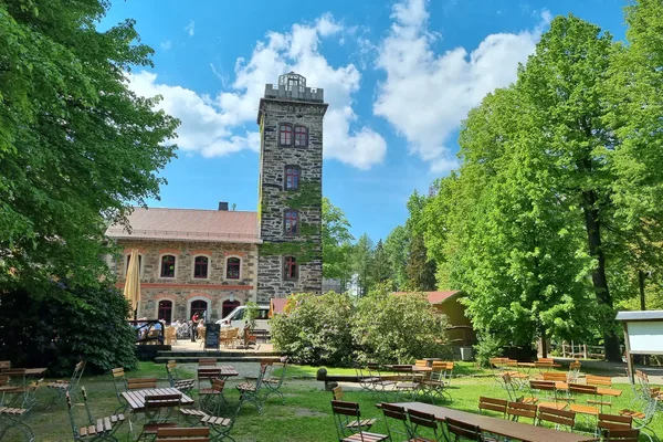 Biergarten im Hof des Butterberg-Berggasthofs mit hohem Steinturm, umgeben von hohen, grünen Bäumen.
