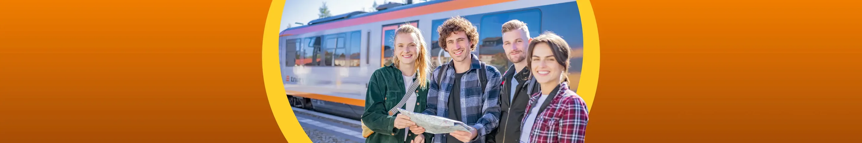 Eine Gruppe von Freunden hält eine Landkarte in der Hand und lacht in die Kamera. Im Hintergrund steht der trilex am Bahngleis.