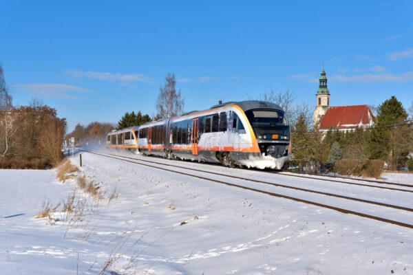 Der trilex fährt durch eine verschneite Landschaft. Im Hintergrund ist eine Kirche zu sehen.