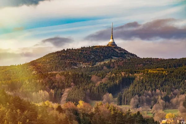 Eine hügelige Landschaft mit Wald. Oben am höchsten Punkt ist der der Fernsehturm von Liberec zu sehen
