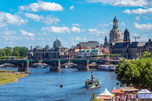 Blick auf einen breiten Fluss, die Elbe, über die eine lange Brücke führt. Im Hintergrund sind die Wahrzeichen Dresdens in der Stadtsilhouette zu sehen.