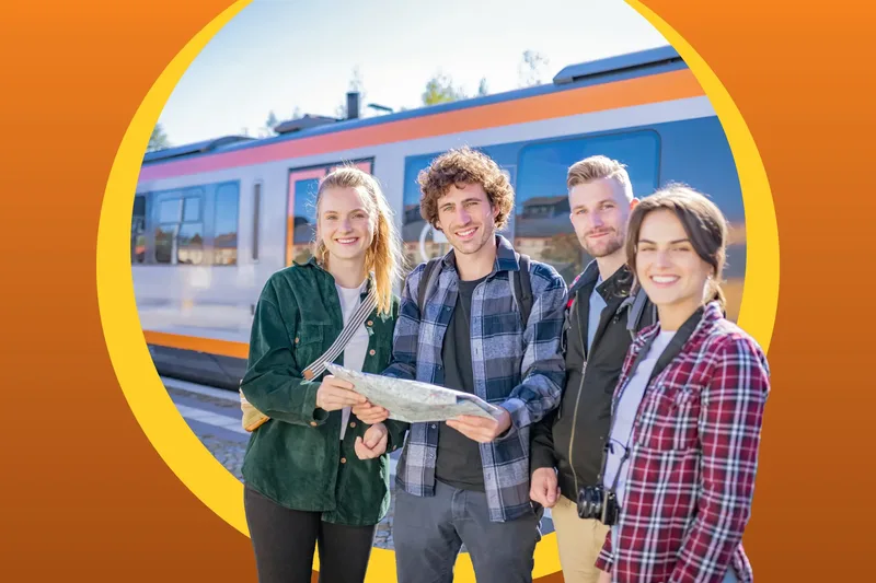 Eine Gruppe von Freunden hält eine Landkarte in der Hand und lacht in die Kamera. Im Hintergrund steht der trilex am Bahngleis.