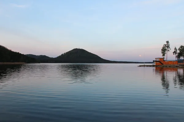 Ein ruhiger See mit leichten Wellen im Sonnenuntergang. Am Horizont sind ein paar kleine Berge zu sehen.