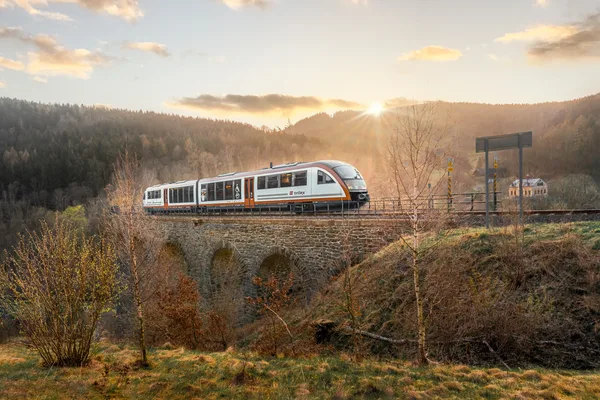 Blick auf das Eisenbahnviadukt in Novina, während ein trilex-Triebwagen beim Sonnenaufgang darüber fährt.