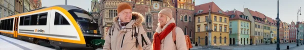 Ein Paar aus Mann und Frau spaziert in Winterklamotten im Vordergrund des Bilds. Im Hintergrund sind der trilex und Häuser in Wroclaw zu sehen.