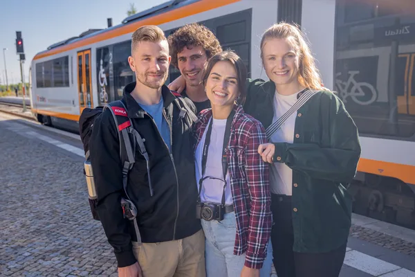 Gruppe von 4 Personen steht am Bahnsteig vor einem trilex.