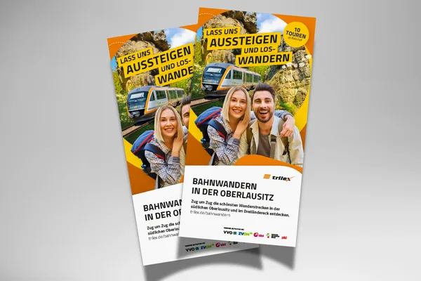 Auf grauem Hintergrund liegen zwei gedruckte Bahnwander-Broschüren des trilex.