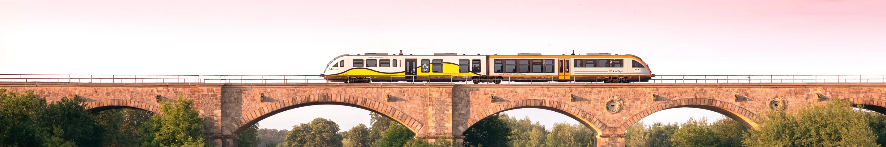 Ein Triebwagen rollt bei Sonnenuntergangsstimmung über eine Brücke