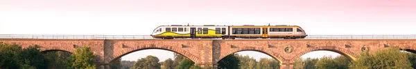 Ein Triebwagen rollt bei Sonnenuntergangsstimmung über eine Brücke