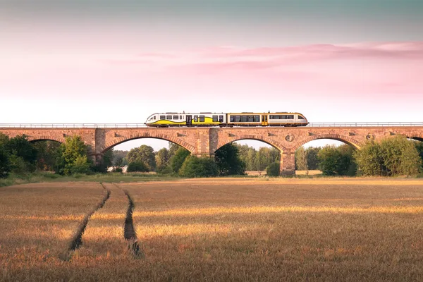 Ein Triebwagen rollt bei Sonnenuntergangsstimmung über eine Brücke