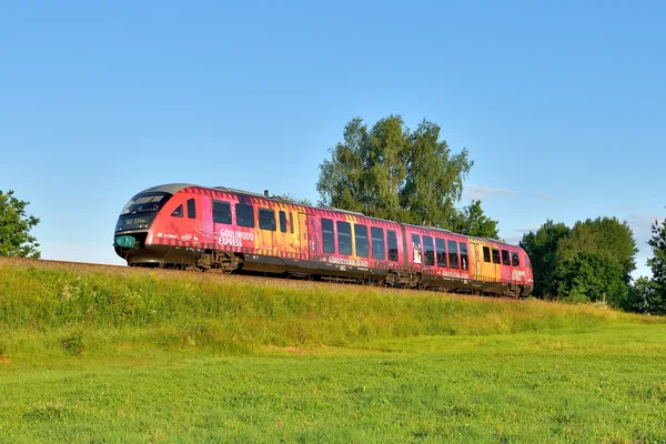 Ein beklebter trielx Triebwagen mit dem Namen "Görliwood Express" fährt umgeben von grünen Wiesen durch die Landschaft.