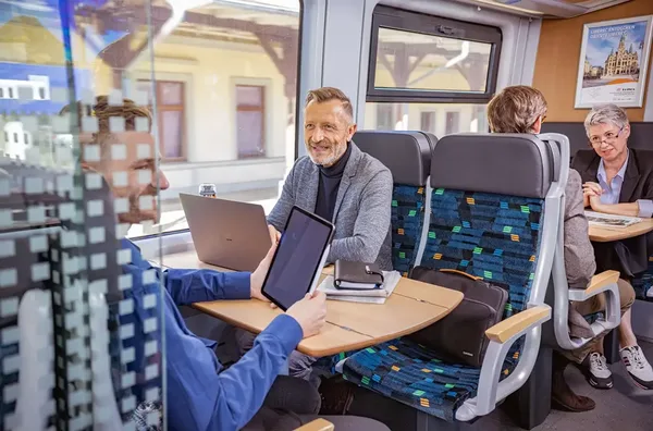 Kilku pasażerów siedzi w czteroosobowych przedziałach w pociągu trilex.