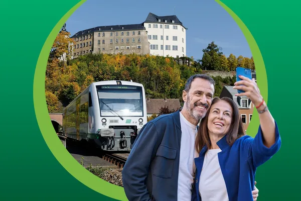 Ein Paar macht ein Selfie. Im Hintergrund fährt die vogtlandbahn an einem Gleis ein.