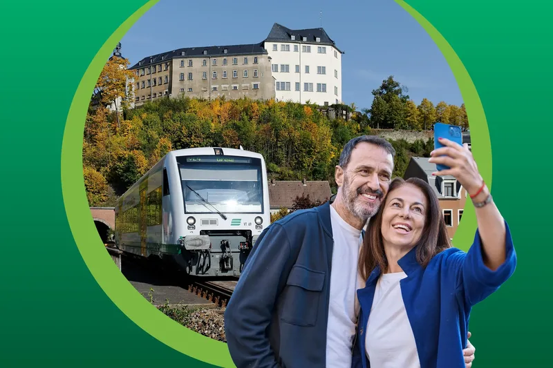 Ein Paar macht ein Selfie. Im Hintergrund fährt die vogtlandbahn an einem Gleis ein.
