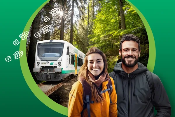 Ein Paar im Wanderoutfit steht im Vordergrund. Im Hintergrund fährt die vogtlandbahn durch die Natur.