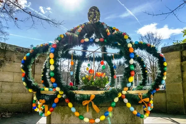 Das Bild zeigt eine hohe Krone aus Ästen, die mit Ostereiern geschmückt ist. Sie ist auf einem Brunnen platziert.