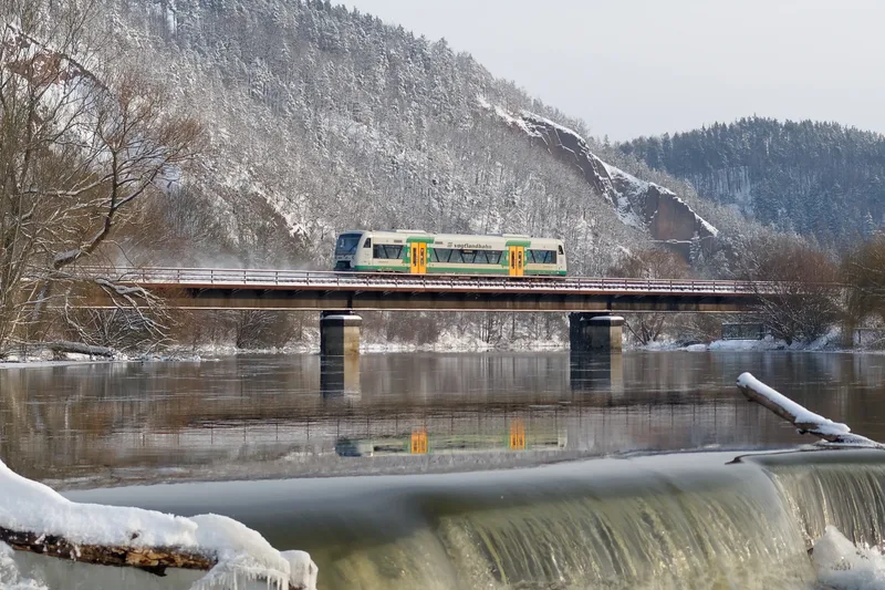 Die Vogtlandbahn fährt im Winter auf einer Brücke über die Weiße Elster und spiegelt sich im Wasser. Fotograf: F. Barteld