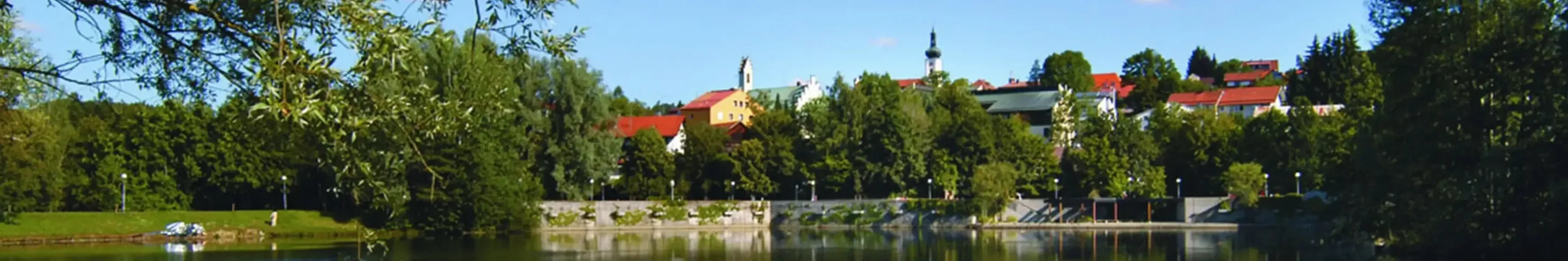 Blick auf eine Stadt mit zwei Türmen, im Vordergrund ist ein See zu sehen.
