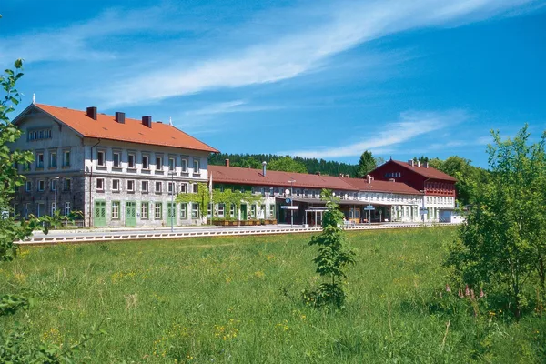 Von einer Wiese aus blickt man auf das Gebäude des Bahnhofs in Bayerisch Eisenstein.