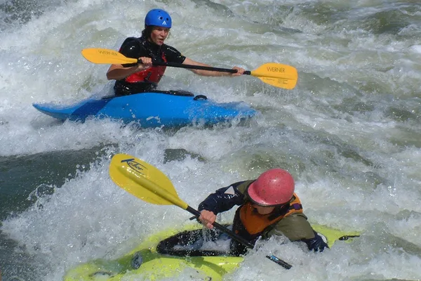 Zwei Kajakfahrer fahren durch turbulentes Wellen und Strömungen.
