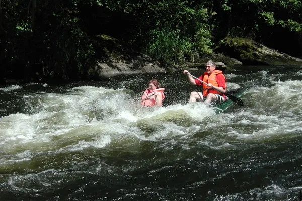 Zwei Personen paddeln mit ihren Kanus durch turbulentes Wasser.
