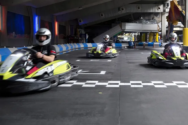 Drei Karts auf einer Indoor-Rennstrecke bei der Zieleinfahrt.