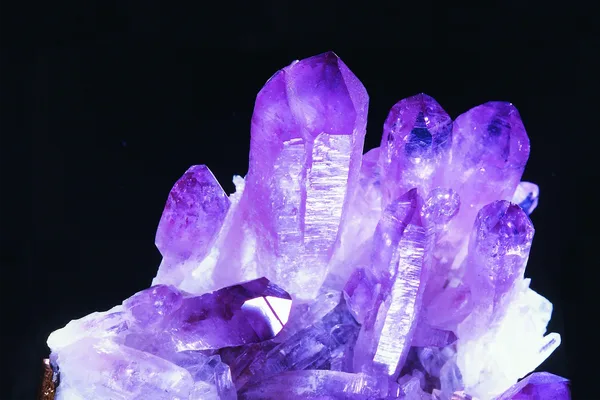 Lilafarbene Kristalle, die sich vor schwarzem Hintergrund türmen.