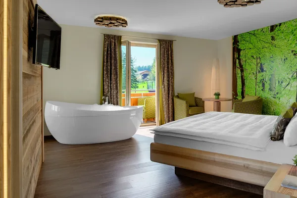 Ein Hotelzimmer mit freistehender Badewanne, Balkon und grüner Waldtapete.