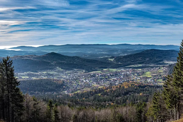 Blick von oben, auf eine Ortschaft, die von vielen Hügeln und Bergen voller Bäume umgeben ist.