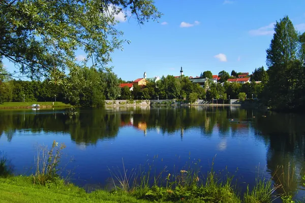 Blick auf eine Stadt mit zwei Türmen, im Vordergrund ist ein See zu sehen.