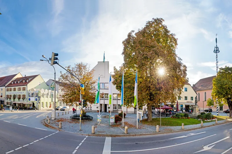 Eine Straßenkreuzung, neben der sich ein kleiner gepflasterter Platz mit einem Café und einer kleinen Wiese befindet.