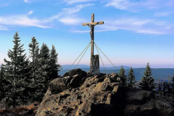Gipfelkreuz auf einem felsigen Gipfel umgeben von Nadelbäumen.