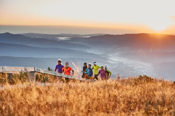 Eine Gruppe Trailrunner läuft bei Sonnenuntergang einen Bergweg nach oben.