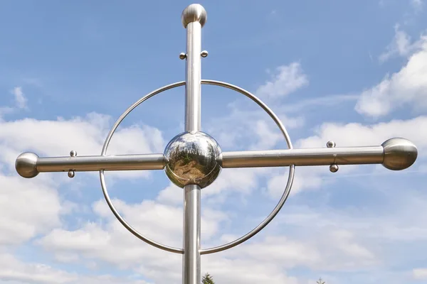 Ein kunstvolles Gipfelkreuz aus hellem Metall mit runden Akzenten.