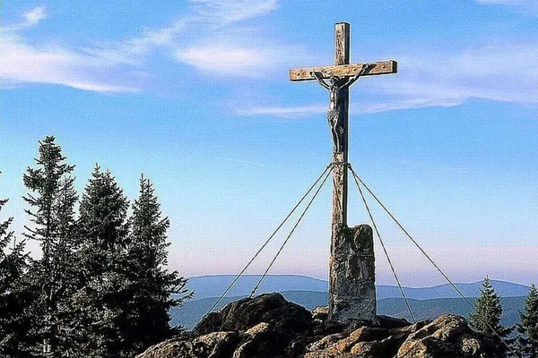 Ein Gipfelkreuz vor blauem Himmel und Ausblick auf den Bayerischen Wald.