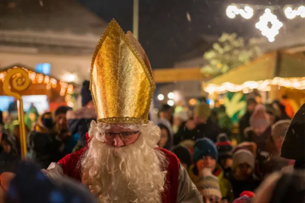 Ein Nikolaus mit langem Bart, Stab und Mütze steht in einer Menschenmenge.