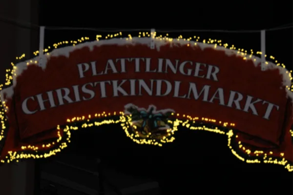 Ein rotes Eingangsschild mit der Beschriftung "Plattlinger Christkindlmarkt", das mit Lichterketten geschmückt ist.