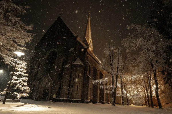 Nächtlicher Blick von unten auf eine imposante Kirche im Schneefall.
