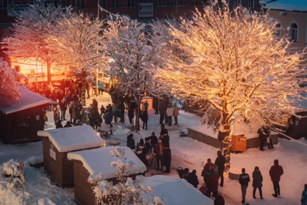 Blick von oben auf einen verschneiten Weihnachtsmarkt mit einigen Besuchern.