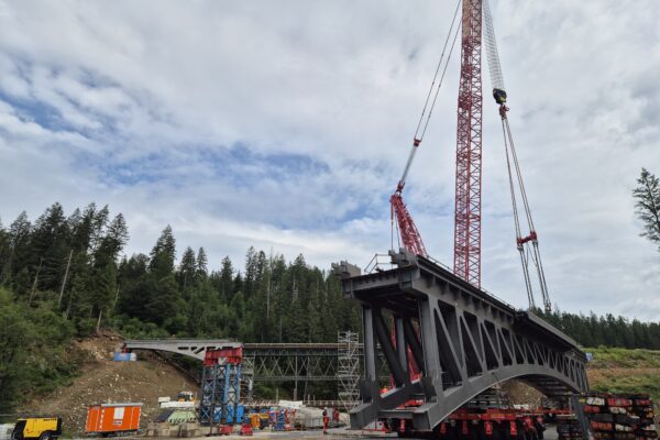 Die komplette neue Nagerlbrücke hängt an einem Spezialkran. Im Hintergrund die alte Brücke.