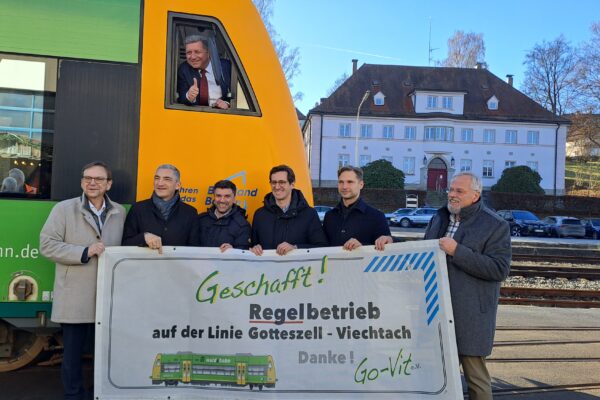Verkehrsminister Christian Bernreiter macht "Daumen hoch" aus dem Führerstand einer waldbahn. Davor stehen Viechtachs Bürgermeister Franz Wittmann, Regens Landrat Ronny Raith, Länderbahn-Geschäftsführer Eugen Rubinstein, die Landtagsabgeordneten Stefan Ebner (CSU) und Toni Schuberl (Grüne) und Wolfgang Schlüter vom Förderverein Go-Vit. Sie halten ein Transparent hoch mit der Aufschrift:"Geschafft! Regelbetrieb auf der Linie Gotteszell-Viechtach. Danke!"