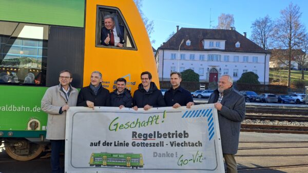 Verkehrsminister Christian Bernreiter macht "Daumen hoch" aus dem Führerstand einer waldbahn. Davor stehen Viechtachs Bürgermeister Franz Wittmann, Regens Landrat Ronny Raith, Länderbahn-Geschäftsführer Eugen Rubinstein, die Landtagsabgeordneten Stefan Ebner (CSU) und Toni Schuberl (Grüne) und Wolfgang Schlüter vom Förderverein Go-Vit. Sie halten ein Transparent hoch mit der Aufschrift:"Geschafft! Regelbetrieb auf der Linie Gotteszell-Viechtach. Danke!"