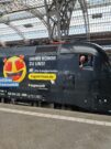 Auf diesem Bild sehen Sie einen schwarzen Zug, aus dem der Triebfahrzeugführer schaut.