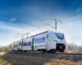 Sie sehen auf diesem Bild den Siemens Mireo Zug von vorn während einer Fahrt. Im Hintergrund sind nicht belaubte Bäume.