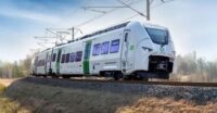 Sie sehen auf diesem Bild den Siemens Mireo Zug von vorn während einer Fahrt. Im Hintergrund sind nicht belaubte Bäume.