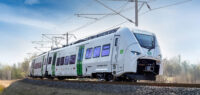 Sie sehen auf diesem Bild den Siemens Mireo Zug von vorn während einer Fahrt. Im Hintergrund sind nicht belaubte Bäume.
