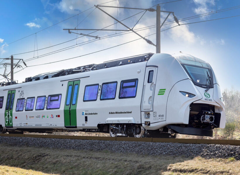 Sie sehen auf diesem Bild den Siemens Mireo Zug von vorn während einer Fahrt. Im Hintergrund sind nicht belaubte Bäume.